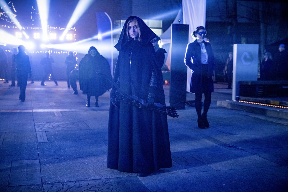 Mia Smoak em uma capa, segurando um arco no The CW