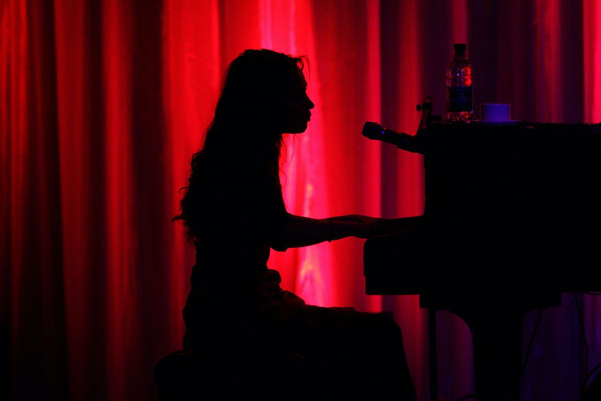 Fiona Apple toca piano em silhueta contra uma cortina vermelha.