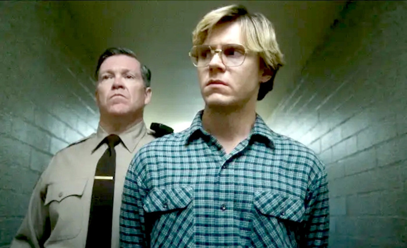   Evan Peters como Jeffrey Dahmer en Netflix's Monster series, being escorted down a hallway by a policeman.