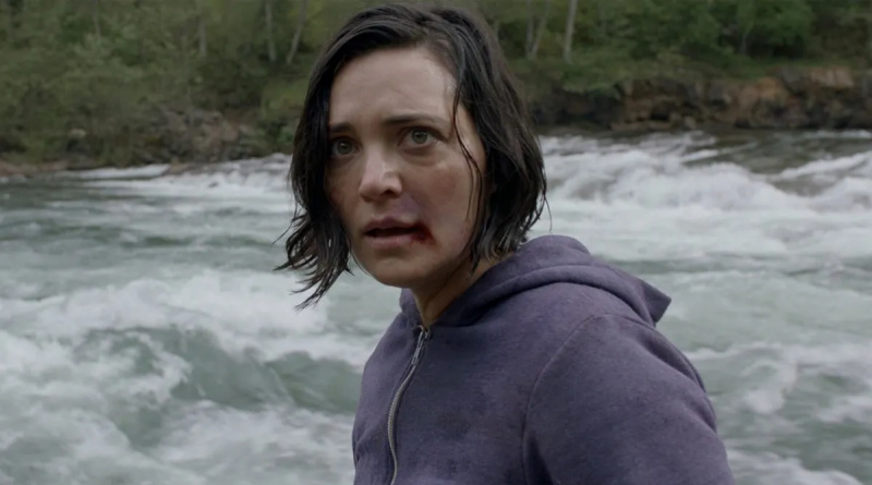  Una mujer con el labio ensangrentado se encuentra frente a un río embravecido.