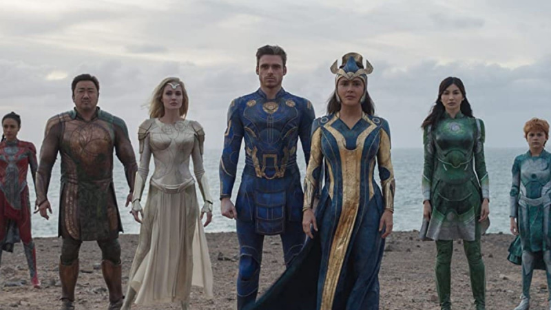  Obsadenie'Eternals' stands on a beach in their superhero outfits.