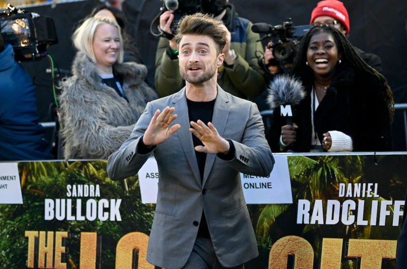  Daniel Radcliffe gestikulerar vilt på röda mattan för The Lost City medan folk skrattar i bakgrunden