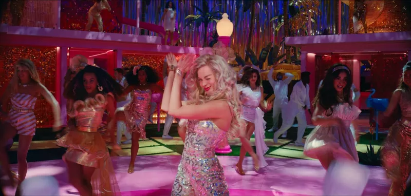  Маргот Роббие's Barbie dancing, holding up her hands and clapping while winking, in the midst of a Barbie dance party in Greta Gerwig's Barbie movie.