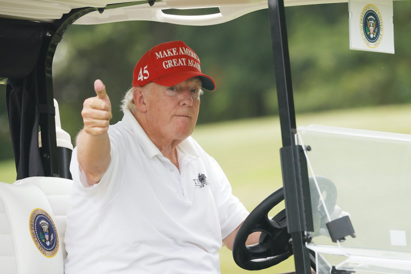   Donald Trump usa un sombrero rojo MAGA mientras conduce un carrito de golf, levanta el pulgar hacia la cámara