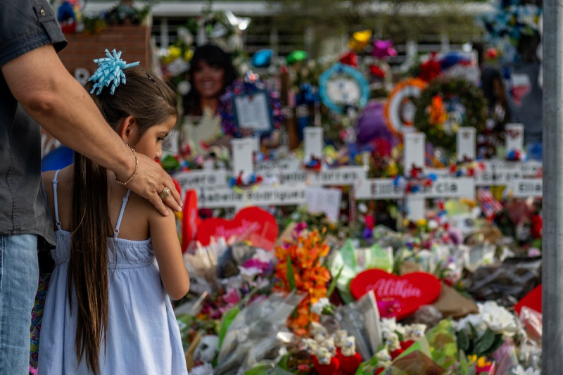   Un hombre y una niña se paran en un monumento a las víctimas del tiroteo en la escuela en uvalde, texas