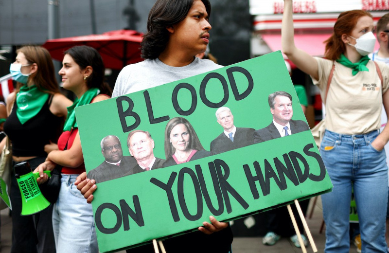   Un manifestante sostiene un cartel con las imágenes de los jueces conservadores de la corte suprema y las palabras"blood on your hands."