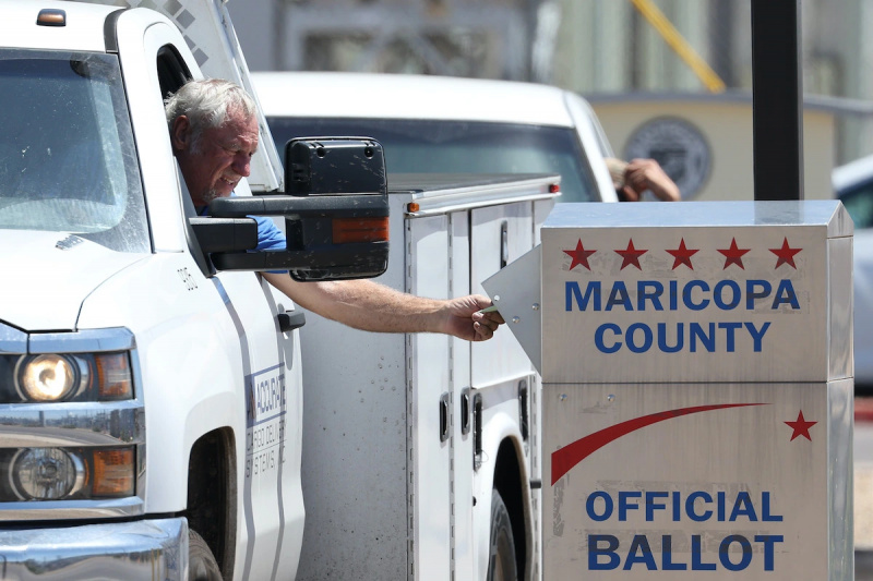  Un anciano blanco se asoma por la ventanilla de su camioneta para depositar una papeleta en un buzón electoral oficial del condado de Maricopa.