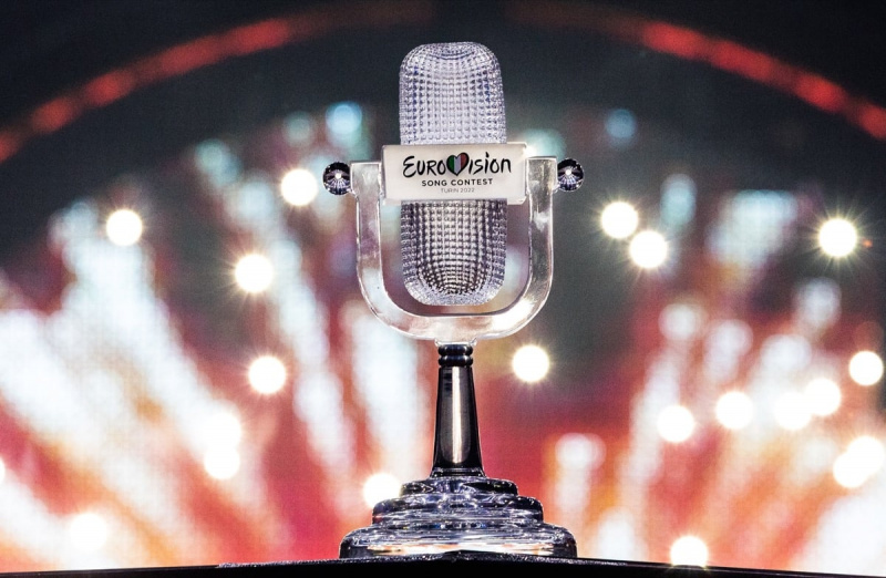   El trofeo de Eurovisión, con forma de micrófono, con un fondo de fuegos artificiales.