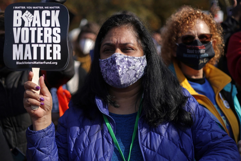   Демонстрант који носи маску за лице држи мали натпис који чита"black voters matter"