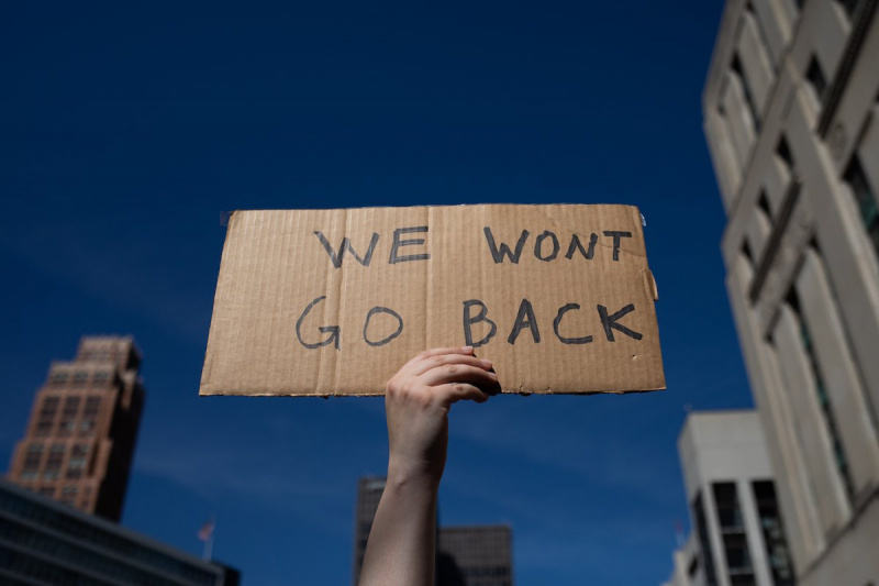  Una mano sostiene un pequeño cartel de cartón escrito a mano contra el fondo del cielo de la ciudad que dice 'Ganamos't go back"