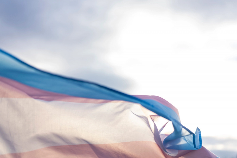  Ružová, biela a modrá transrodová vlajka vlajúca s oblohou za ňou.