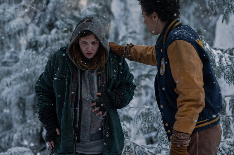   Shauna se od bolečine prepogne, medtem ko se Taissa dotakne njene rame. Oni're in the woods with snow falling.