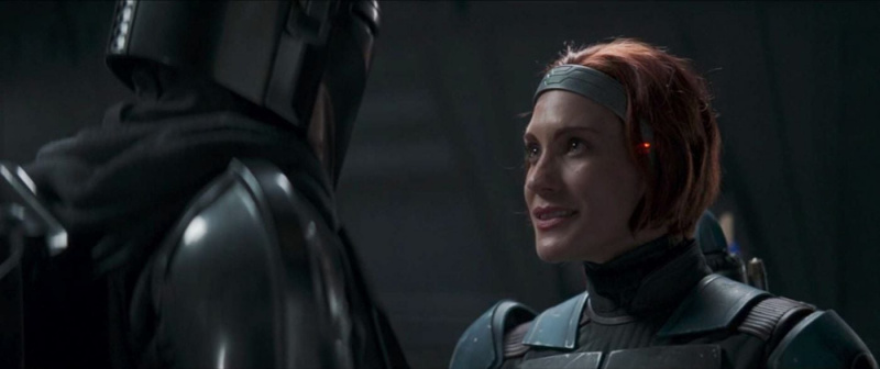   Katee Sackhoff como Bo-Katan Kryze en una escena de'The Mandalorian' on Disney+. We see her from the shoulders up. She's in her armor, but her helmet's off, so we see her face, grey headband, and chin-length red hair. She's looking up at Din Djarin.