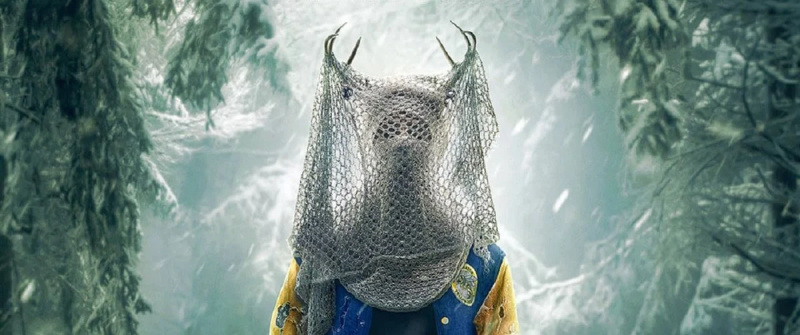   Kraljica rogovja iz Yellowjacktsa: postava, oblečena v rogovje, univerzitetno jakno in nogometno mrežo, ki zakriva njihov obraz, stoji na zasneženem ozadju.